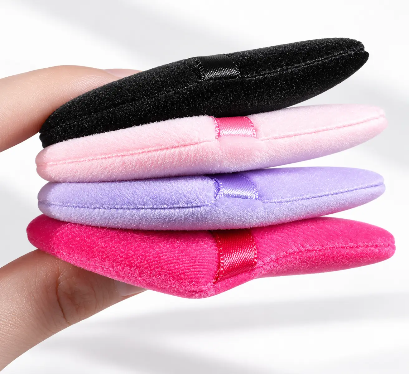 Side profiles of triangle powder puffs showing the padded body and stitched edges
