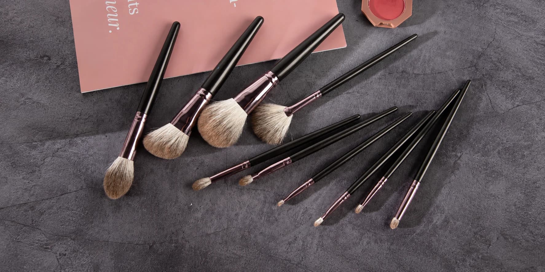 Makeup brush assortment with black handles and rose-tone ferrules on a gray surface