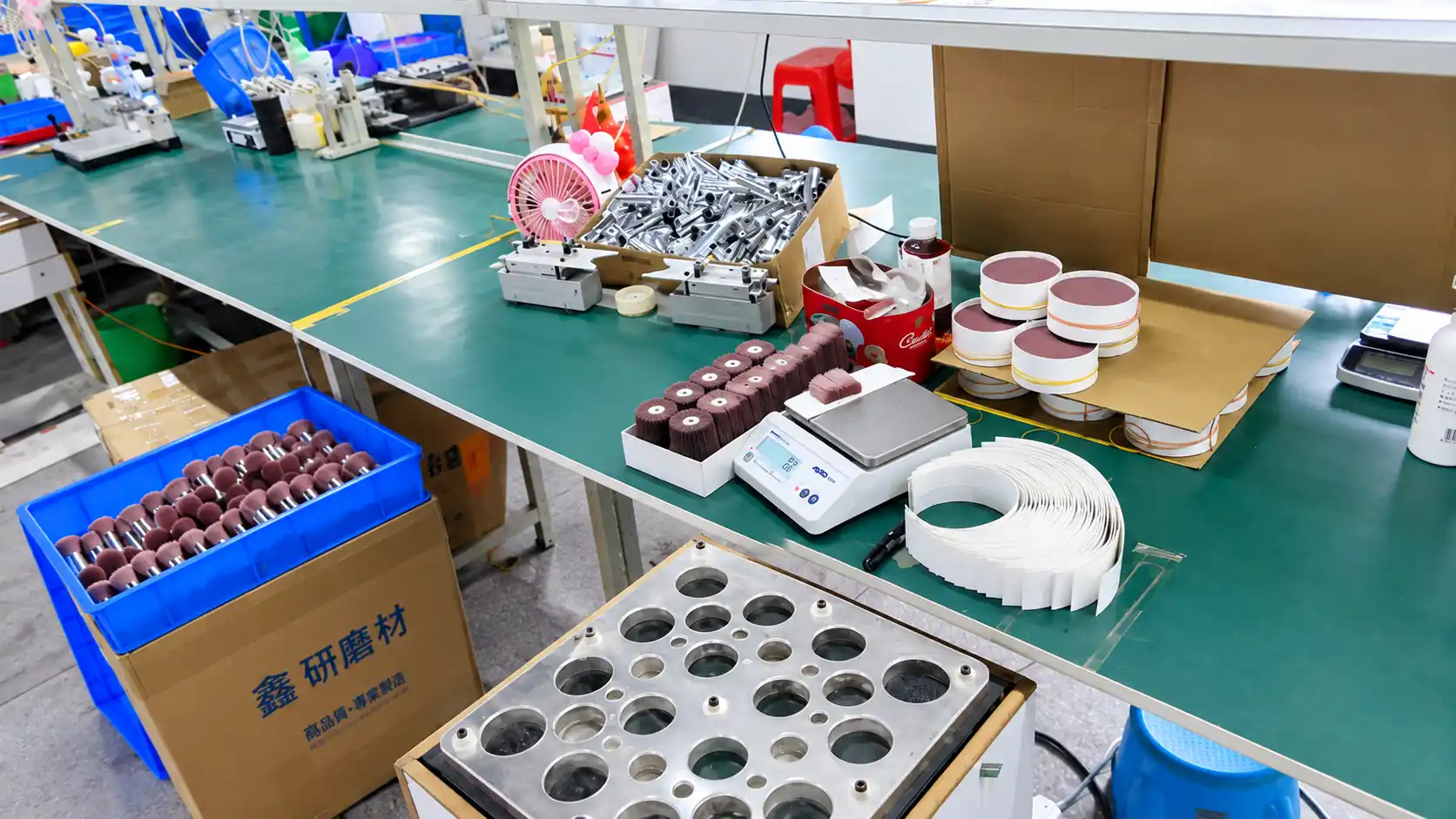 Makeup brush components, blue trays, measuring scale and tools on a green production workstation