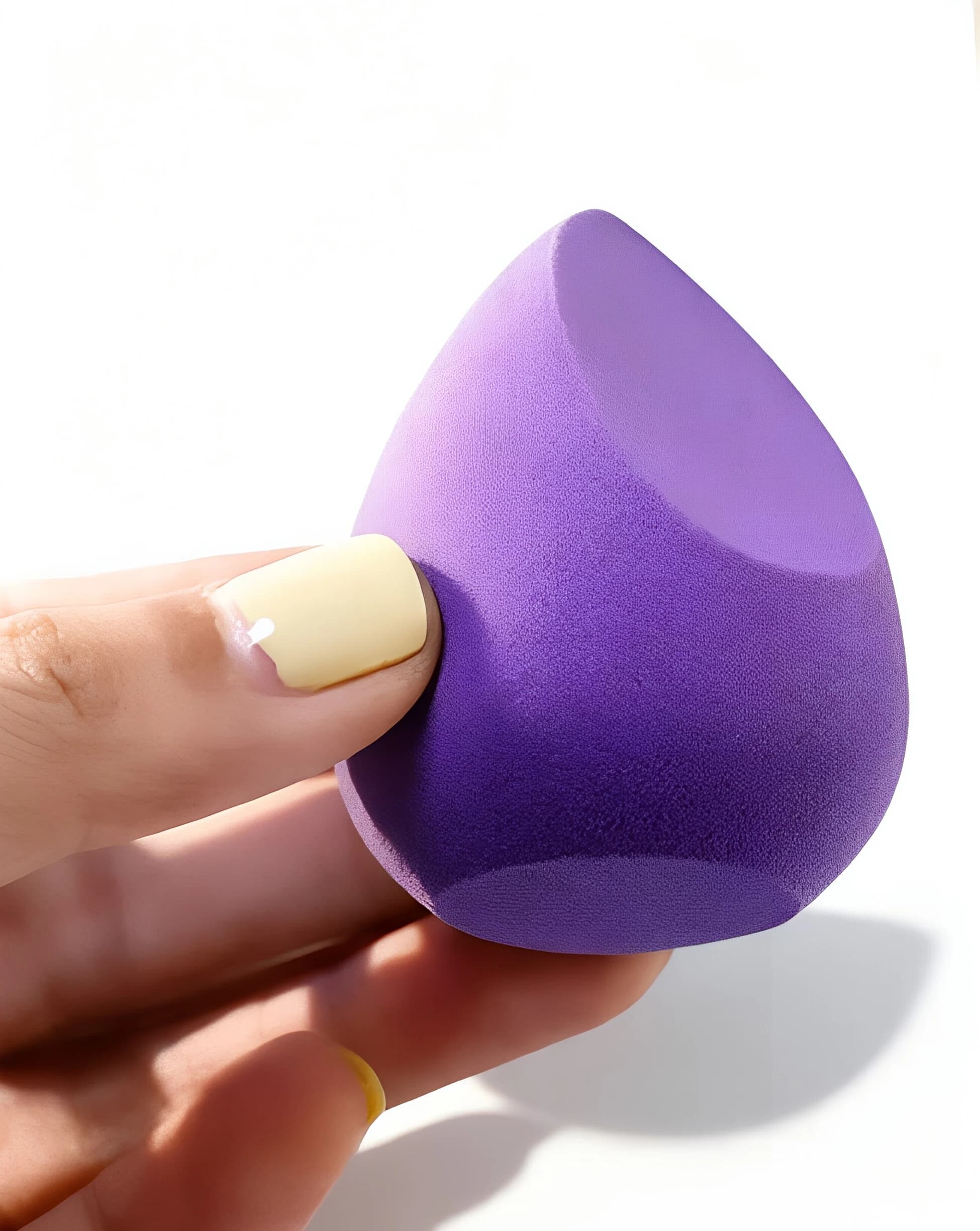 Purple angled makeup sponge held in a hand, showing its slant-cut face and rounded side